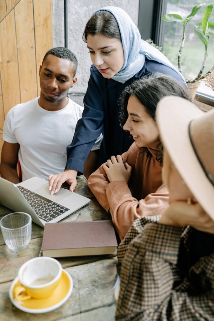 A diverse group of young adults collaborating on a project in a cozy, sunlit cafe environment.